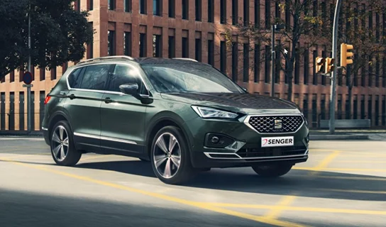 Ein grau-grüner SEAT Tarraco fährt über eine asphaltierte Straße in einer Stadt.