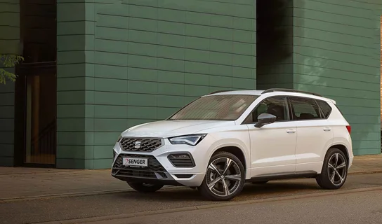 Ein weißer SEAT Ateca steht auf einer asphaltierten Straße vor einem grünen Gebäude.