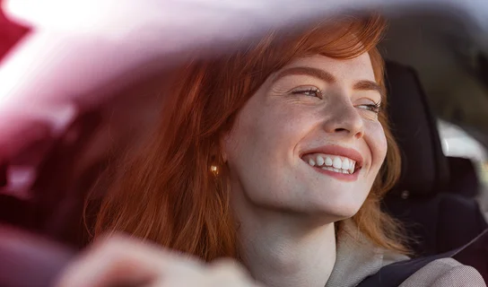 Eine Frau sitzend und lachend in einem Auto.