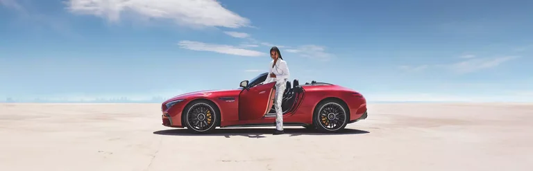 Roter Mercedes AMG C 43 in Seitenansicht in einer Wüstenlandschaft. Aus der Fahrertür des Cabrio steigt eine Frau in weißem Anzug.