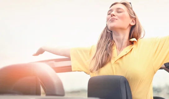 Frau auf dem Beifahrersitz eines Cabriolets, die ihre Arme ausstreckt.