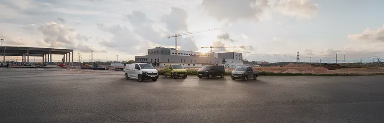 Vier Volkswagen Nutzfahrzeuge Transporter Modelle auf einem Parkplatz mit einer Baustelle im Hintergrund.